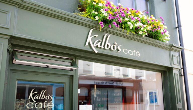 Exterior of Kalbo's Café with green façade, large windows, and a flower box with colourful blooms above the sign.